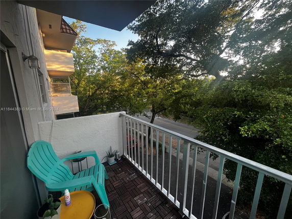 View from a balcony facing a tree-lined street with some adjacent building balconies visible.
