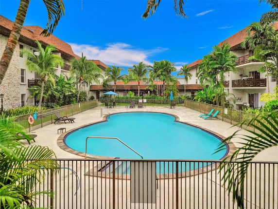 Outdoor swimming pool surrounded by palm trees and apartment buildings.