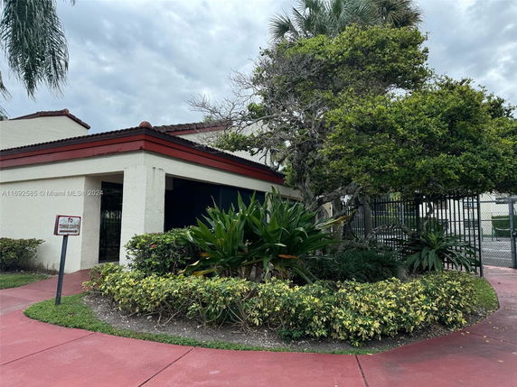 Front view of a building with a tennis court sign and surrounding greenery.