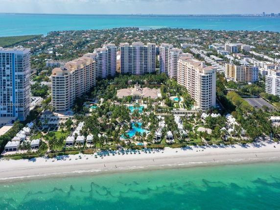 Panoramic view of large beachfront resort with multiple high-rise buildings and swimming pools, overlooking the ocean.