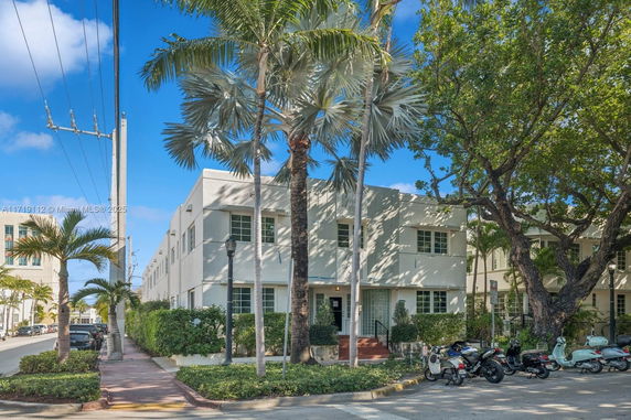 Front view of a two-story building with palm trees and parked scooters.