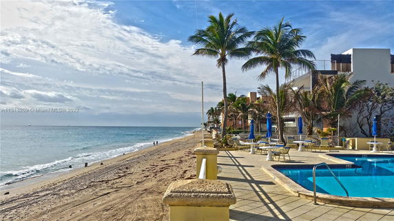 A beachfront area with a swimming pool and palm trees, overlooking the ocean.