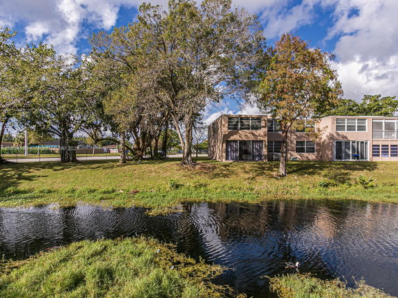 Back view of a two-story house with large windows and a pond in the foreground.