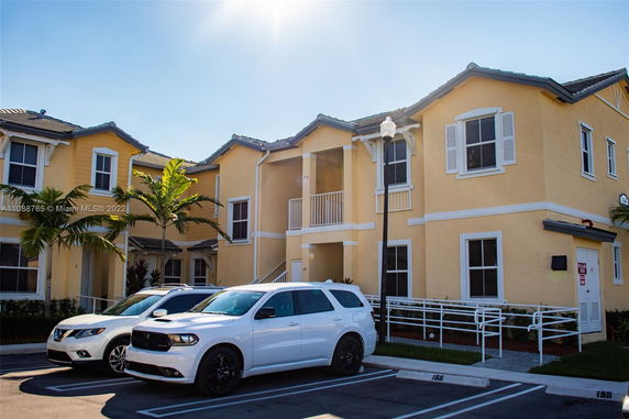 Parking area in front of a two-story yellow building with two vehicles parked.