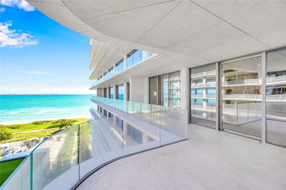Panoramic view from a balcony overlooking the ocean, with modern building architecture and glass railings.