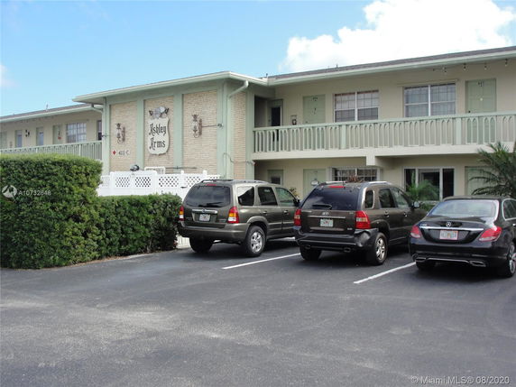 Front view of a two-story residential building with a parking area containing several cars.