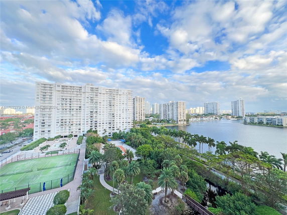 View of high-rise buildings near a waterfront with tennis courts and palm trees.