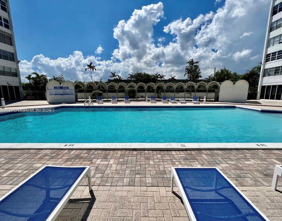 Outdoor swimming pool area with lounge chairs and adjacent buildings.
