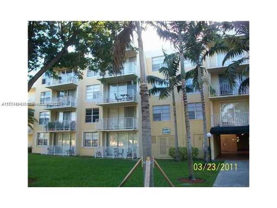 Front view of a multi-story apartment building with balconies and palm trees.