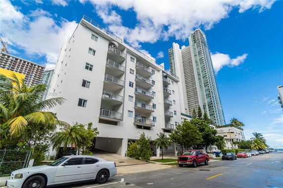 Front view of a multi-story apartment building with balconies and parking area at the base.