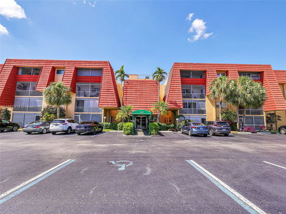 Front view of a multi-story building with red roofs and parking area.