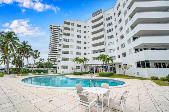 View of a multi-story residential building with balconies and a swimming pool in front.