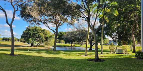 A scenic view of a grassy area with trees and a small pond under a clear blue sky.