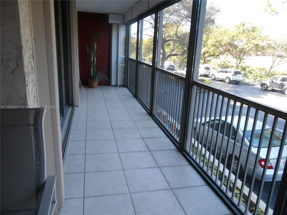 Balcony with tiled floor and metal railings overlooking parked cars and trees.