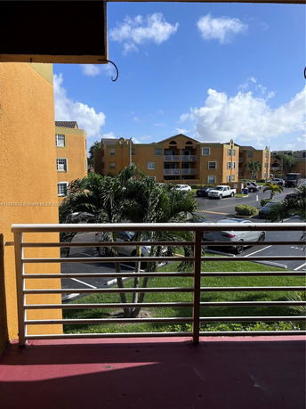 View from a balcony overlooking parking area and nearby buildings.