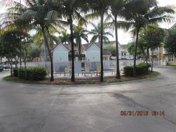 Outdoor swimming pool area surrounded by a fence and palm trees, with adjacent residential buildings.