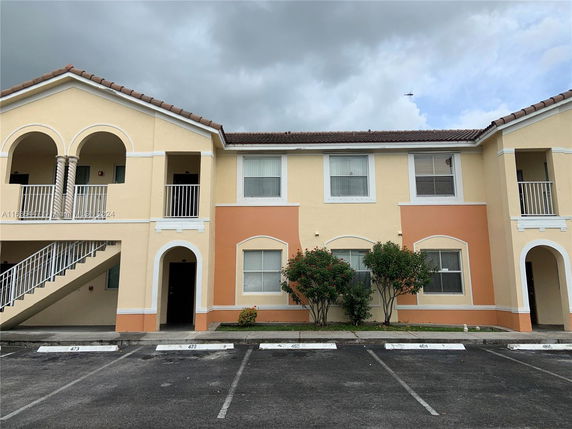 Front view of a two-story residential building with arches and parking area in front.