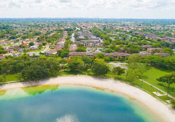 Aerial view of residential area with houses and apartments near a lake and greenery.