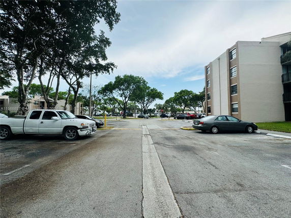 Outdoor parking area with several cars near a multi-story building.