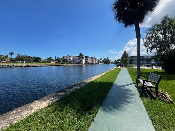 View of buildings along a waterway with a grassy area and bench in the foreground.