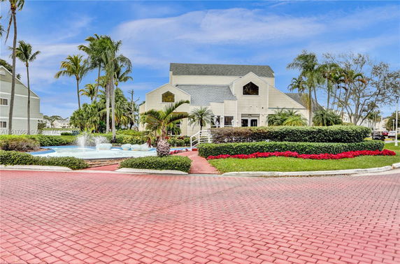 Front view of a building with multiple roof lines, surrounded by landscaped gardens and a water fountain.