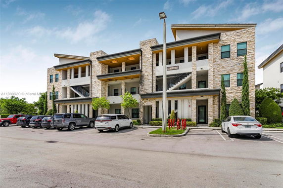 Front view of a multi-story building with stone facade and parking area in front.