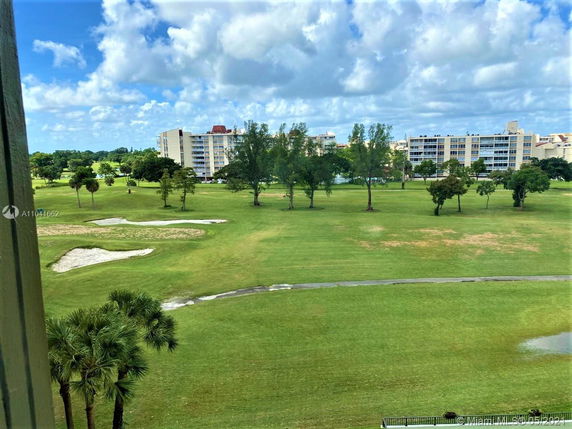View of a grassy landscape with sand traps, trees, and apartment buildings in the distance.