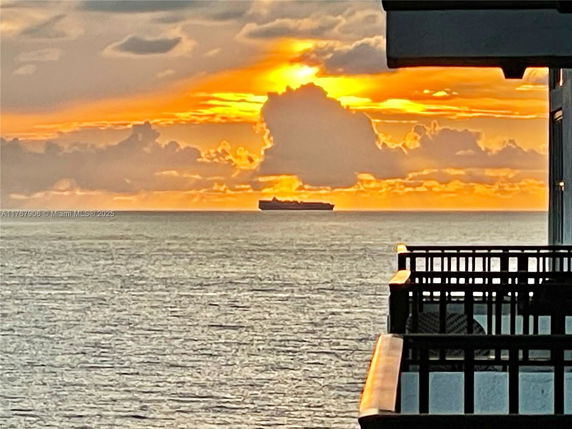 View of the ocean and a ship at sunset from a building balcony.