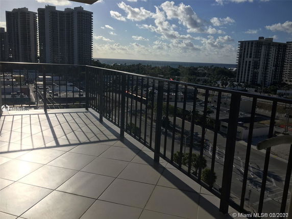 Panoramic view from a balcony with tall buildings and ocean in the distance.