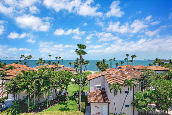 View of coastal residential buildings with terracotta roofs and ocean in the background.