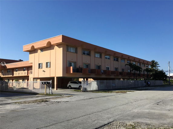 Front view of a multi-story residential building with parking and fenced perimeter.