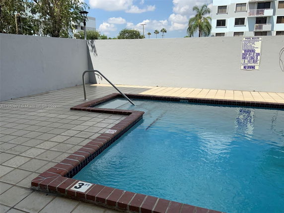Outdoor view of a swimming pool with tiled surroundings and a safety handrail.