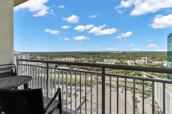 Panoramic view from a balcony overlooking a cityscape with buildings and green areas.