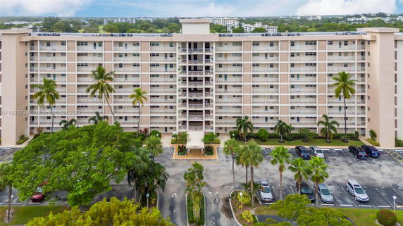 Front view of a multi-story apartment building with balconies and a parking area in front.