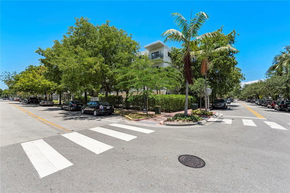 Street view with cars parked along the road and trees lining the sidewalk.