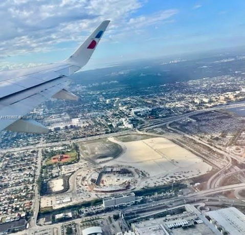 Aerial view of an urban area with residential and commercial buildings, roadways, and open spaces; partial airplane wing visible.