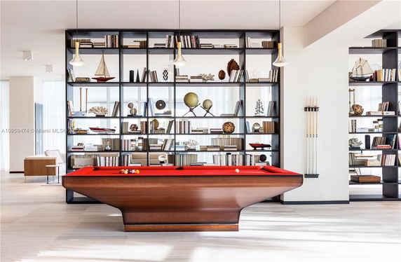 Interior view of a recreation area with a red pool table and bookshelves filled with books and decorative items.