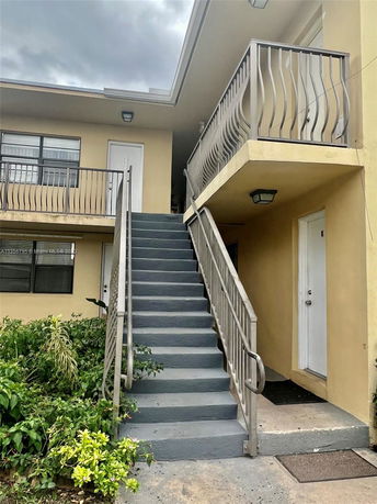Front view of a two-story building with stairs leading to the upper level and beige exterior walls.