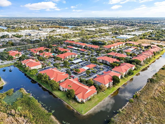 Aerial view of a residential complex with red-roofed buildings surrounded by trees and water bodies.