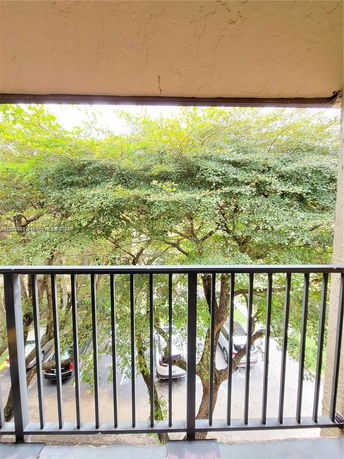 View from a balcony showing trees and cars parked below.