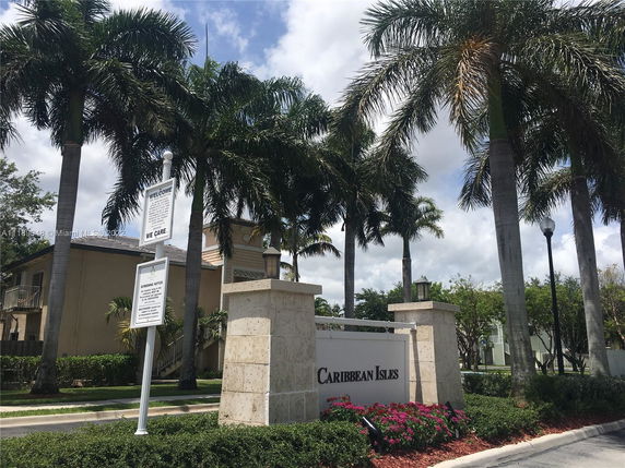 Front view of a building complex entrance with sign and palm trees.