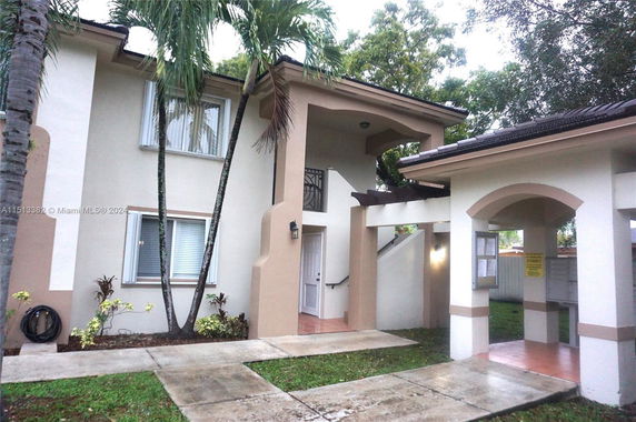 Front view of a two-story house with an arched entryway and palm trees.