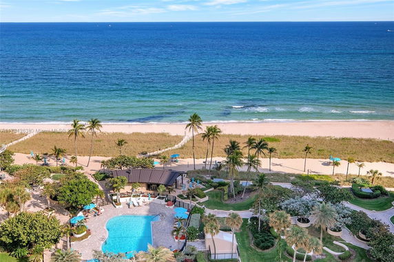 Aerial view of a beachside area with a swimming pool and lush gardens overlooking the ocean.