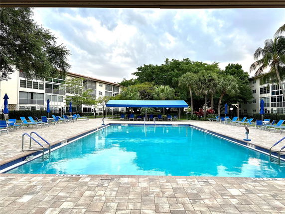 View of a swimming pool area surrounded by residential buildings and trees.