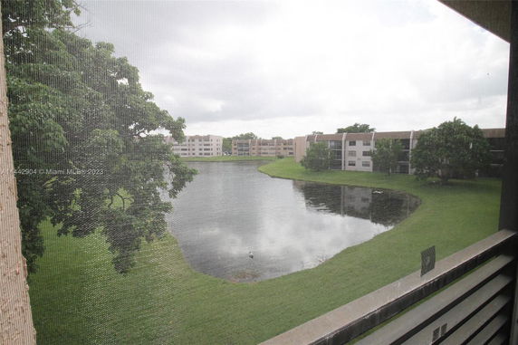 View of multiple apartment buildings near a water body surrounded by grass and trees.