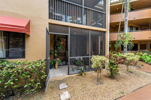 Front view of a multi-story building with screened balconies and surrounding plants.