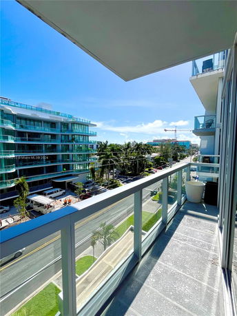 Balcony view overlooking a street with modern buildings and palm trees.