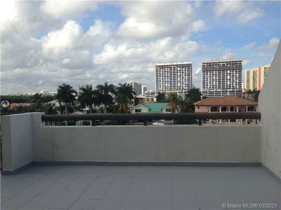 Rooftop terrace with a railing, offering a view of nearby buildings and palm trees.