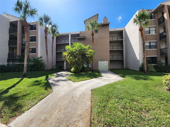 Front view of a multi-story residential building with balconies and palm trees.