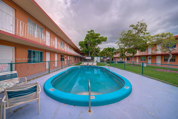 Outdoor swimming pool area surrounded by a two-story building.